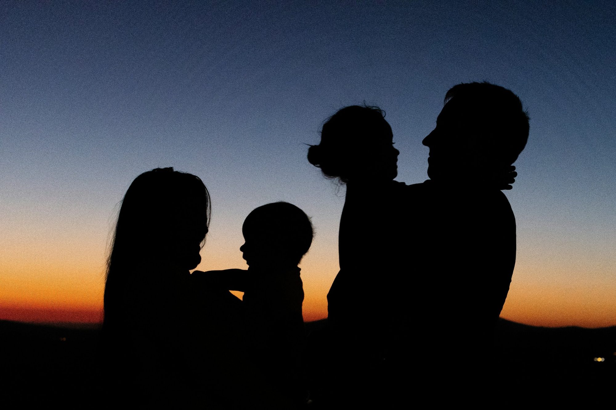 A family in silhouette against the evening sky, parents holding their little ones